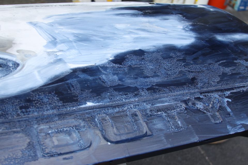 Close-up of a dark vehicle part with white paste applied, showing embossed text