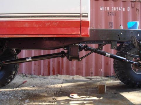 1982 Ford F-100 - Side view under a red-and-white pickup showing a freshly painted black rear axle and driveshaft with long tubular triangulated four-link ar…