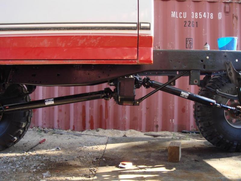 Black rear axle with tubular four-link suspension under a red and white lifted pickup