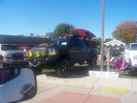 1989 Ford Bronco - Modified pickup truck with kayak on roof rack parked next to other vehicles at an outdoor event.