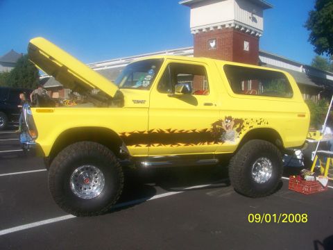 1989 Ford Bronco - A yellow Ford Bronco with custom graphics and a lifted suspension is parked outdoors with its hood open.