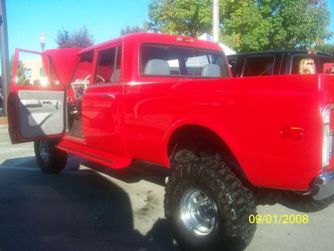 1989 Ford Bronco - A red extended cab pickup truck is parked outdoors with its doors open, showing off its interior and lifted suspension.