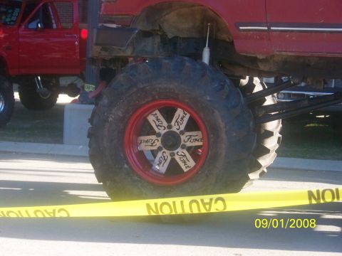 1989 Ford Bronco - A lifted red Ford Bronco with custom wheels and large tires is parked next to another red truck.