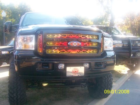 1989 Ford Bronco - A black Ford F-Series truck with a custom flame grille is parked next to another truck.