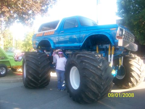 1989 Ford Bronco - Blue monster truck, possibly a modified Ford Bronco, with a person and a green Jeep in the background.
