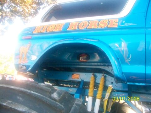 1989 Ford Bronco - A blue monster truck with custom graphics is shown from the side, large tires and suspension components.