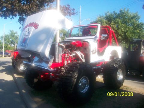 1989 Ford Bronco - A heavily modified Jeep with custom graphics on the hood and a bright red roll cage is displayed with its engine exposed.