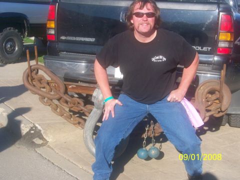1989 Ford Bronco - A man poses with heavy chains attached to the rear of a black Chevrolet Silverado pickup truck.