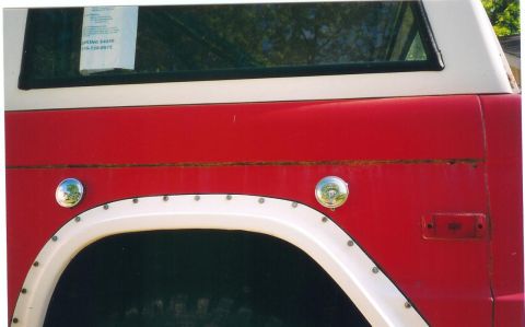 1974 Ford Bronco - The side of a red and white 1974 Ford Bronco is visible, with a white fender flare and a circular fuel cap.
