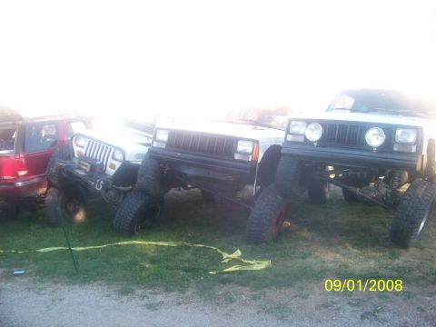 1989 Ford Bronco - Several modified Jeeps are parked on a grassy area, with a red SUV visible on the far left.