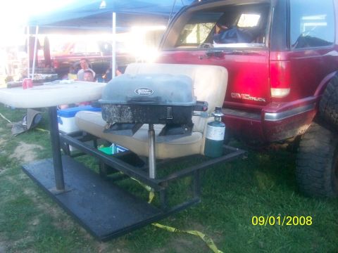 1989 Ford Bronco - A red GMC SUV is parked outdoors with a portable grill and table setup attached to its rear.