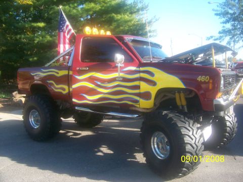 1989 Ford Bronco - Customized red pickup truck with flame graphics and an American flag displayed at an event.
