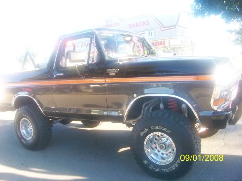 1989 Ford Bronco - This lifted Ford Bronco has a distinctive orange stripe and chrome wheels, parked in front of a food stand.