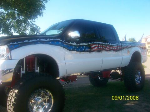 1989 Ford Bronco - Custom lifted pickup truck displays patriotic American flag graphics along its side.