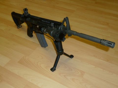 1992 Ford Mustang - Assault rifle with bipod and flashlight on wooden floor.