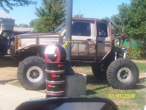 1989 Ford Bronco - A heavily modified truck with oversized tires and a roll cage is displayed outdoors.