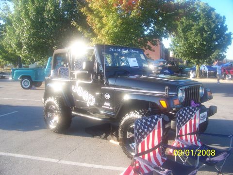 1989 Ford Bronco - A black Jeep Wrangler is parked outdoors, with American flag chairs set up in front of it.