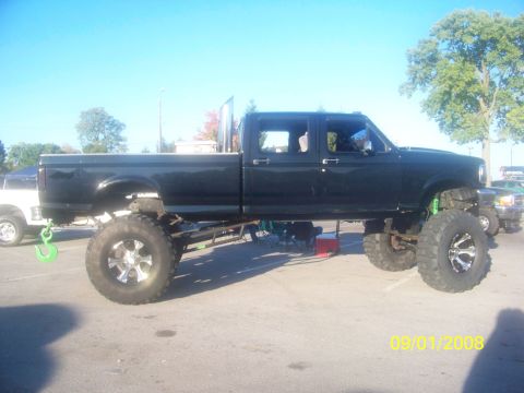 1989 Ford Bronco - A heavily modified black pickup truck with oversized tires is parked outdoors on a sunny day.