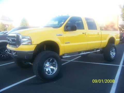 1989 Ford Bronco - Yellow Ford F-350 pickup truck with lifted suspension and chrome wheels, parked on asphalt.