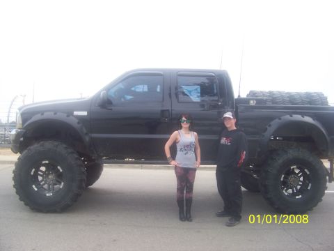 1989 Ford Bronco - A heavily modified black Ford Super Duty pickup truck is shown with two people posing beside it.