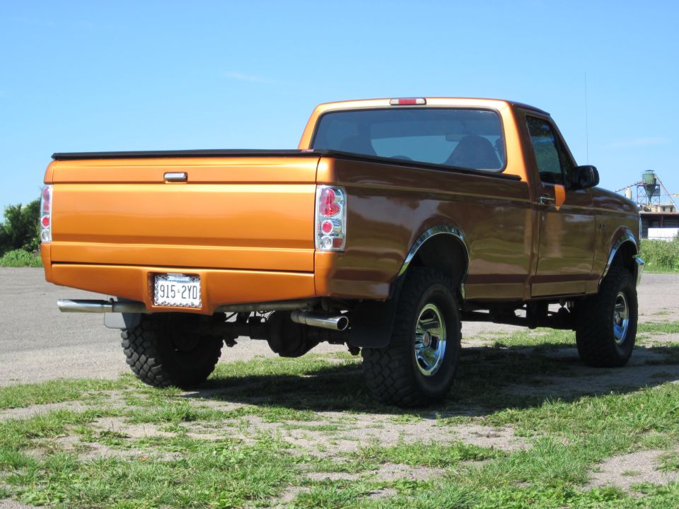 Orange 1995 Ford F-150 pickup truck, rear 3/4 view. Lifted with large tires