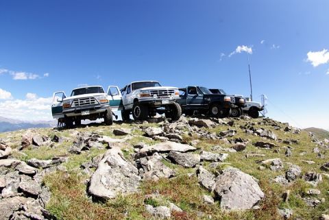 1995 Ford Bronco - Multiple Ford trucks are parked on a rocky hilltop with a clear blue sky above.