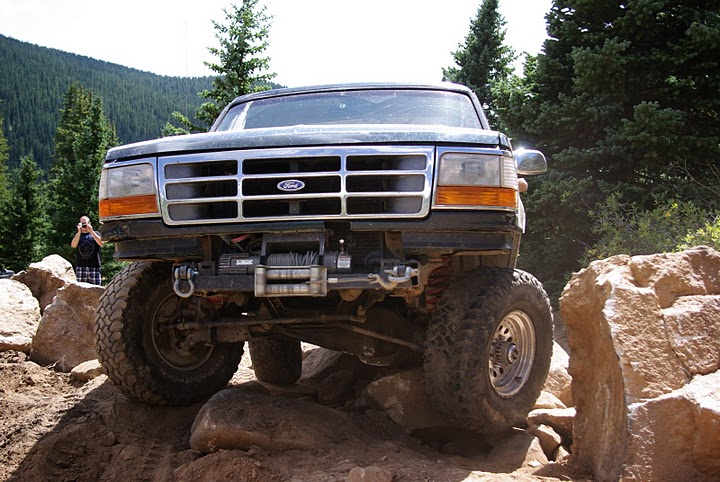 Dark green lifted Ford Bronco with front winch straddling boulders on rocky trail