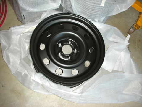 2004 Ford Crown Victoria - A black steel wheel, likely a spare or an upgrade part, is shown wrapped in protective material.
