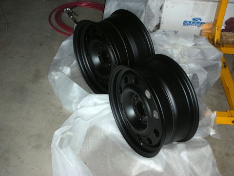2004 Ford Crown Victoria - Two black steel wheels are shown, likely for a vehicle upgrade, with workshop items in the background.