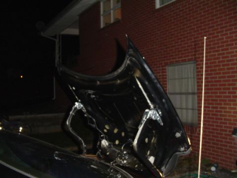 1999 Ford Taurus - The underside of an open car hood is visible at night, with a brick house in the background.