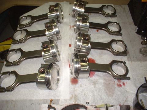 1969 Ford Mustang - A set of eight pistons with connecting rods, likely for an engine rebuild, are visible on a surface stained with oil.