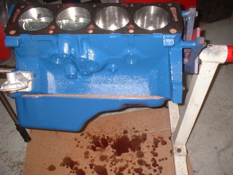 1969 Ford Mustang - Engine block with pistons visible, mounted on a stand with oil stains on the floor.