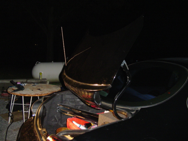 Open trunk of a black car at night, showing contents and a large white propane tank in the background