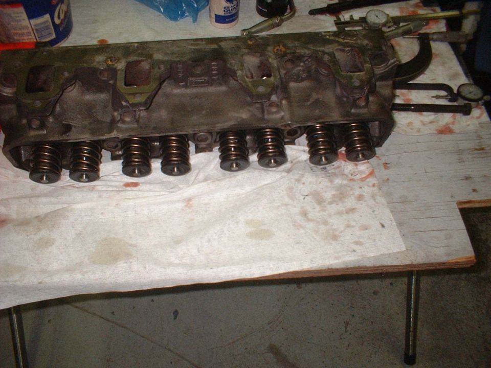 Engine cylinder head with visible valve springs on a workbench with paper towels and tools