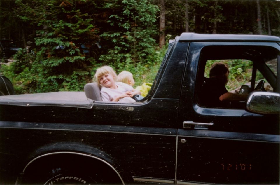 Black 1995 Ford Bronco with two children in the open rear seat, driver visible