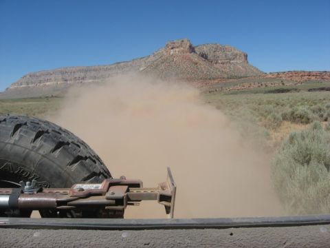 1995 Ford Bronco - A vehicle's spare tire and jack are visible as it kicks up a large dust cloud in a desert landscape.