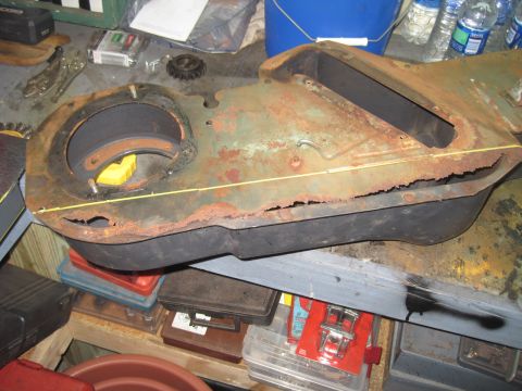 1979 Ford Bronco - This rusted metal part is on a workbench, surrounded by various tools and supplies.