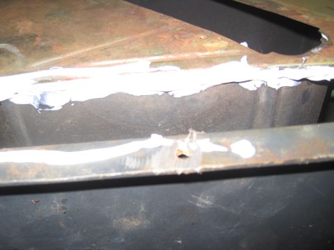 1979 Ford Bronco - Detail of a corroded metal section with sealant and a hole, likely a repair area.
