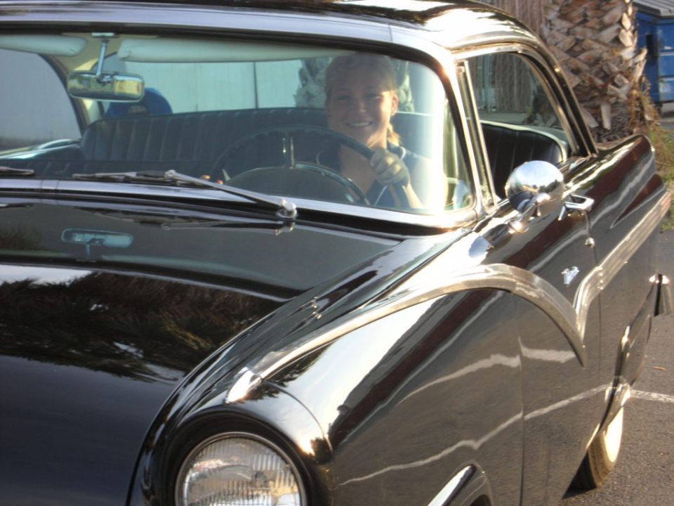 Black 1956 Ford Fairlane coupe with chrome trim, driver visible through windshield