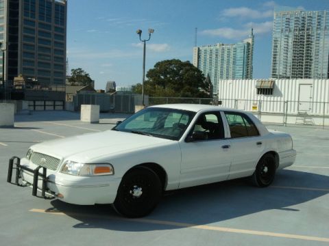 1998 Ford Crown Victoria - A white sedan with a push bar is parked in an urban lot.