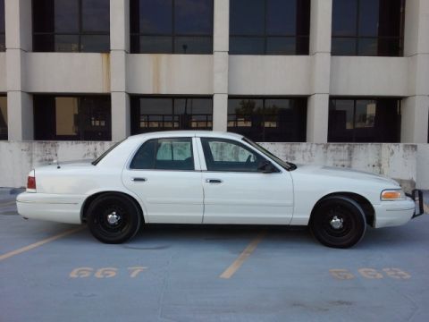 1998 Ford Crown Victoria - A white 1998 Ford Crown Victoria sedan is parked in a lot, viewed from the side with black wheels.