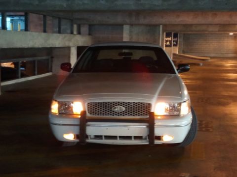 1998 Ford Crown Victoria - Front view of a white 1998 Ford Crown Victoria, equipped with a push bar and its lights illuminated.