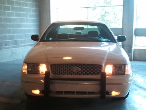 1998 Ford Crown Victoria - A white Ford Crown Victoria with a push bar is parked head-on in a garage.