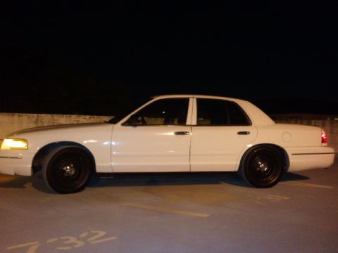 1998 Ford Crown Victoria - A white 1998 Ford Crown Victoria is parked on a concrete surface at night, viewed from the side.