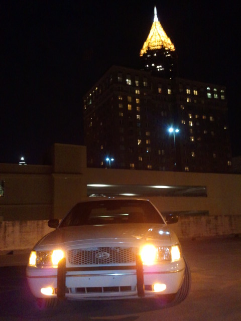 1998 Ford Crown Victoria - Front view of a 1998 Ford Crown Victoria parked at night with a building illuminated in the background.