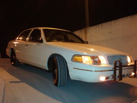 1998 Ford Crown Victoria - A white 1998 Ford Crown Victoria is parked at night, showing its front three-quarter view with headlights on.