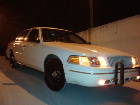 1998 Ford Crown Victoria - A white 1998 Ford Crown Victoria is parked at night with its headlights illuminated.