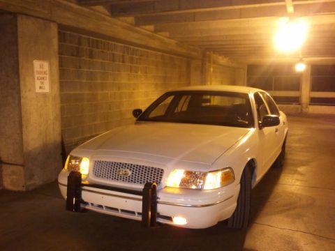 1998 Ford Crown Victoria - A white 1998 Ford Crown Victoria is parked in a garage, showing its front end and push bumper.
