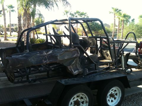 1966 Ford Bronco - A severely damaged vehicle frame, likely an off-road buggy, sits on a trailer under palm trees.
