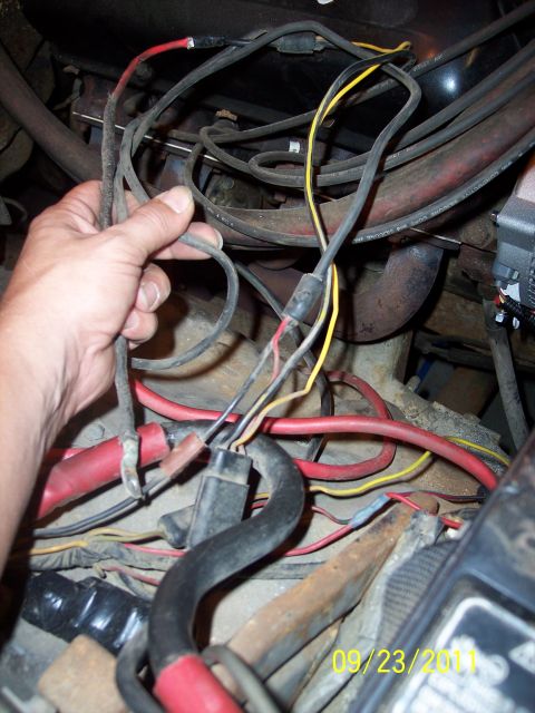 1973 Ford F-250 - A close-up view of a vehicle's engine bay shows a hand manipulating electrical wiring near the exhaust manifold.